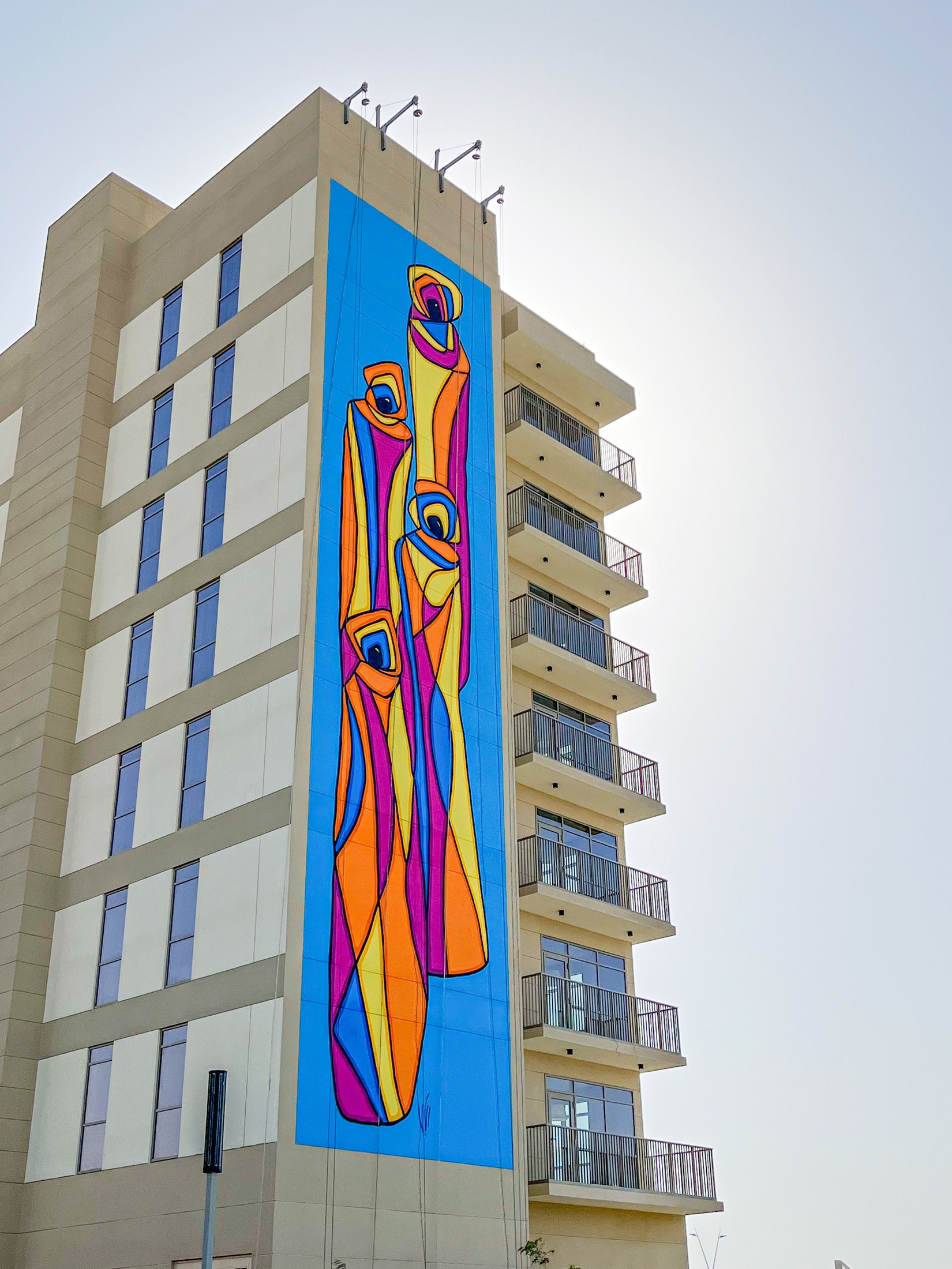 Rabab Tantawy’s completed blue, orange and pink figurative mural across a full Aldar building facade