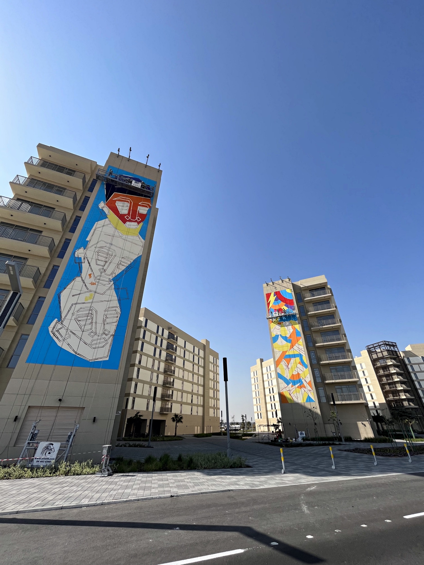 Two mural teams working in parallel across neighbouring Aldar buildings