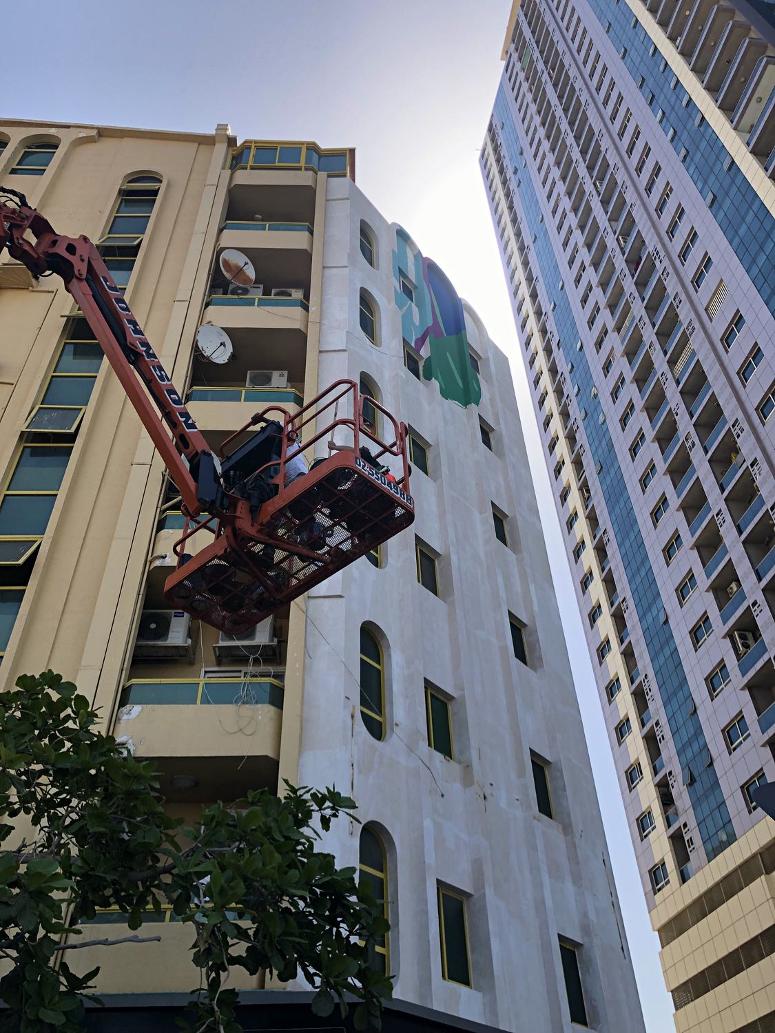 Boom lift positioned beside the Ajman building as the mural work begins