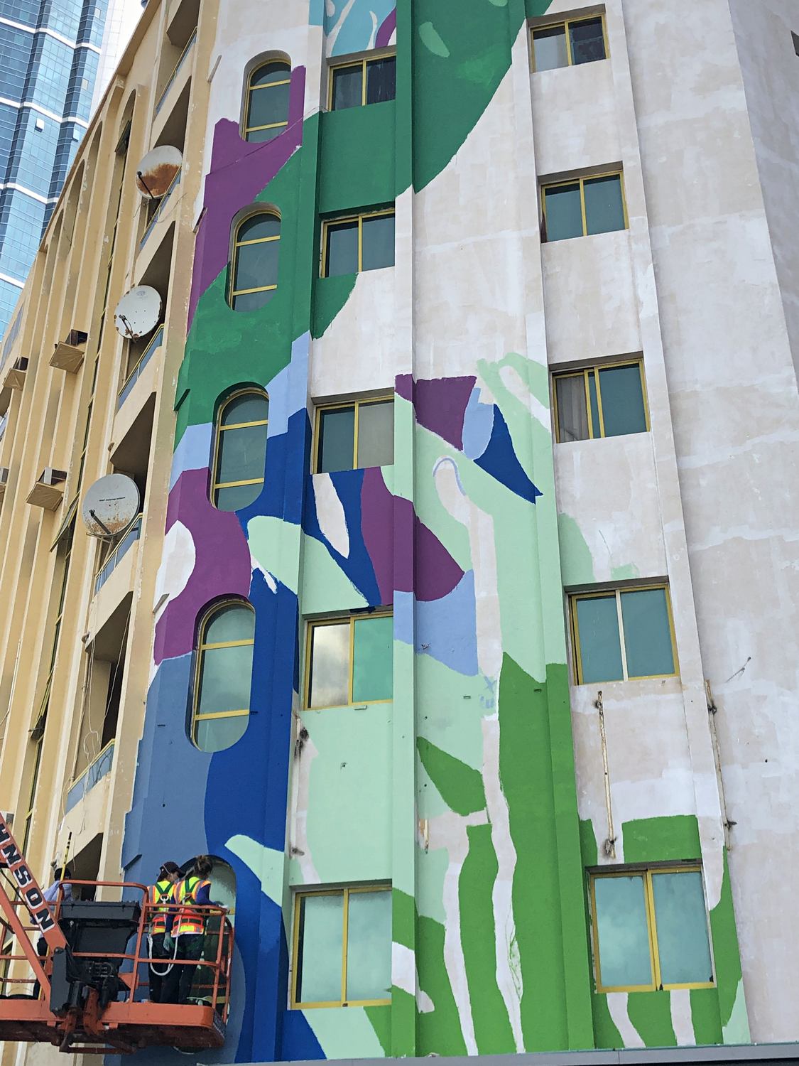Ajman mural developing across the facade with the artist working from a lift
