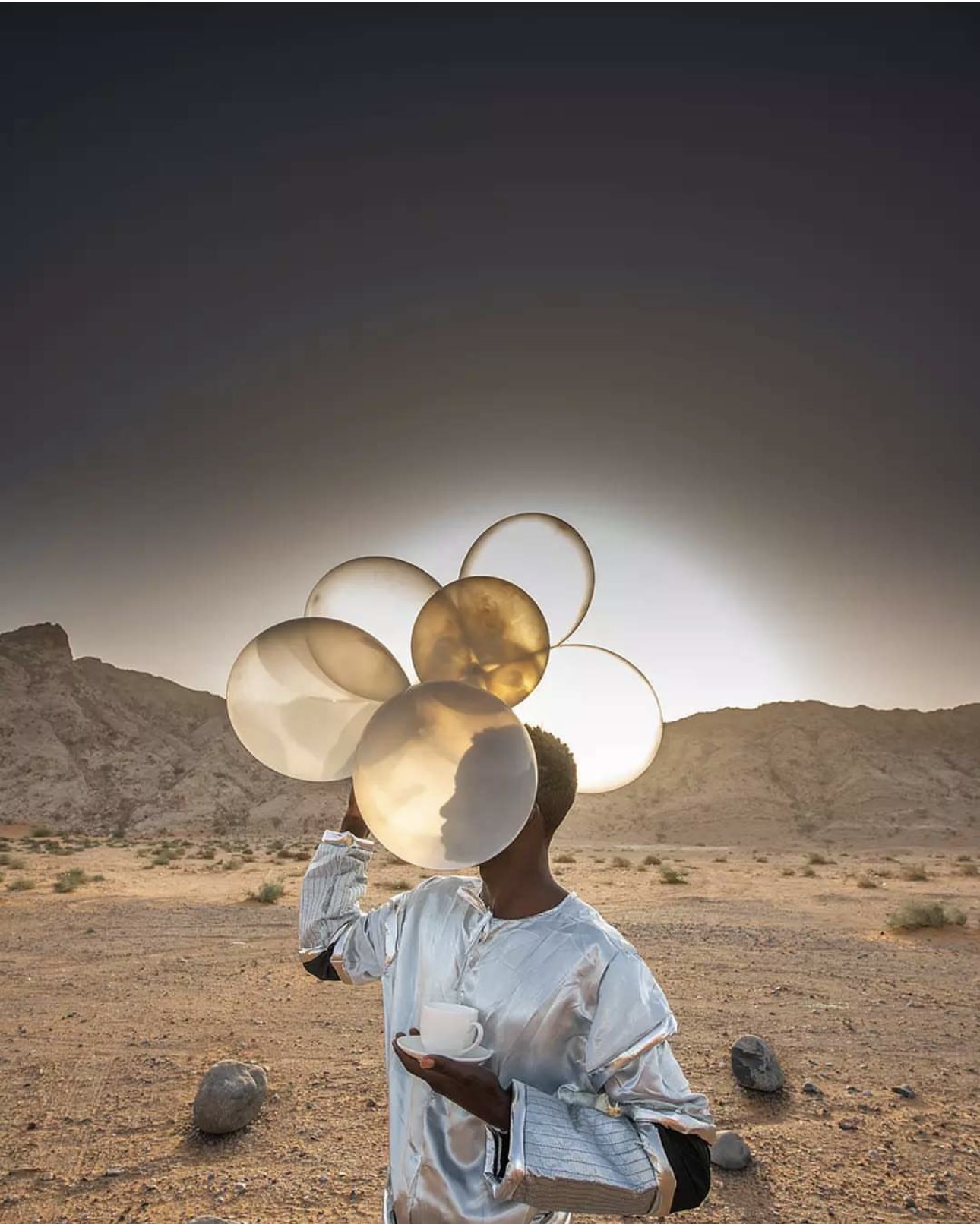 Editorial campaign image featuring a figure carrying translucent balloons in a desert landscape
