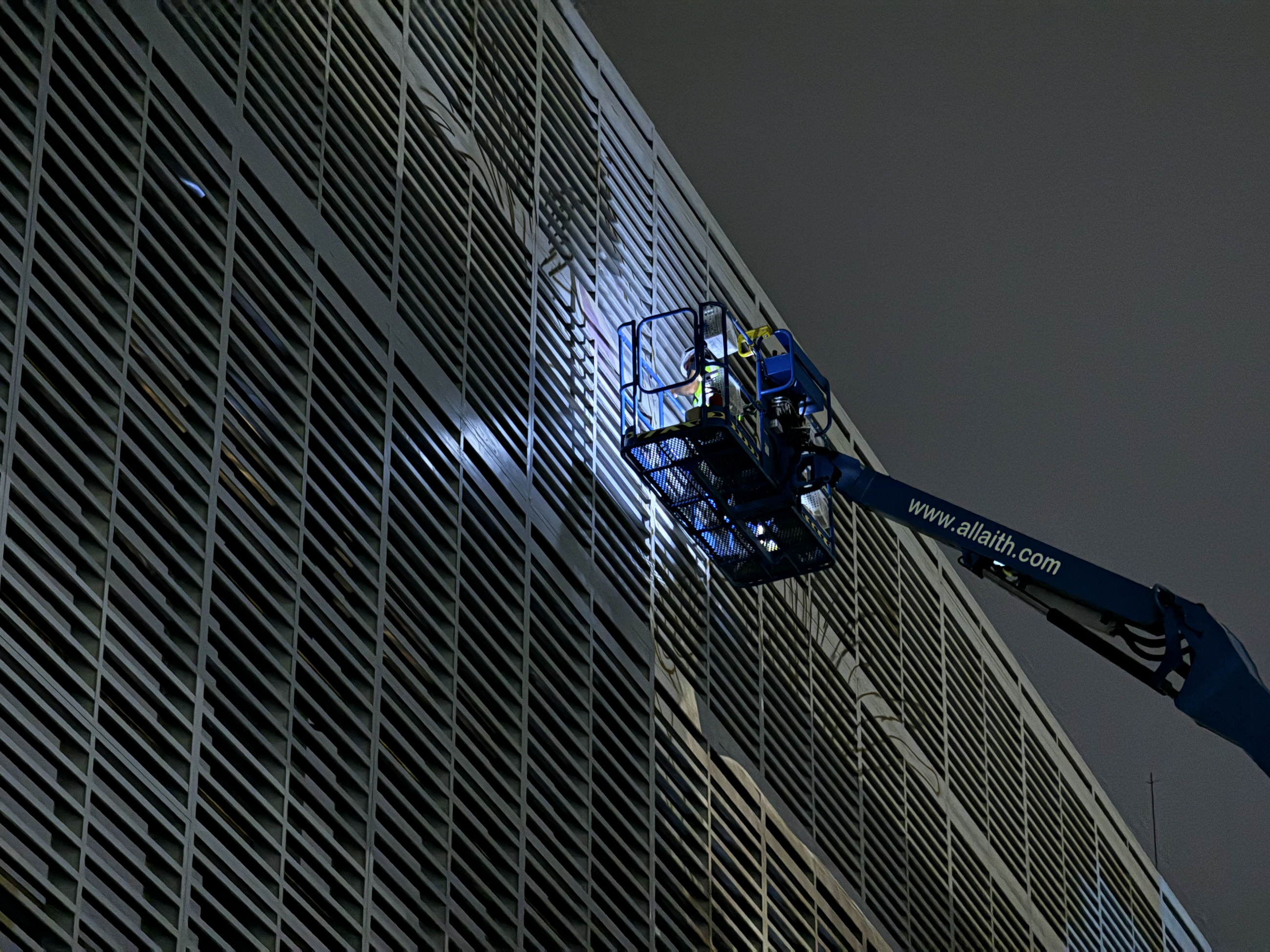 A specialist mural crew illuminated at height against the Tabreed louvres at night
